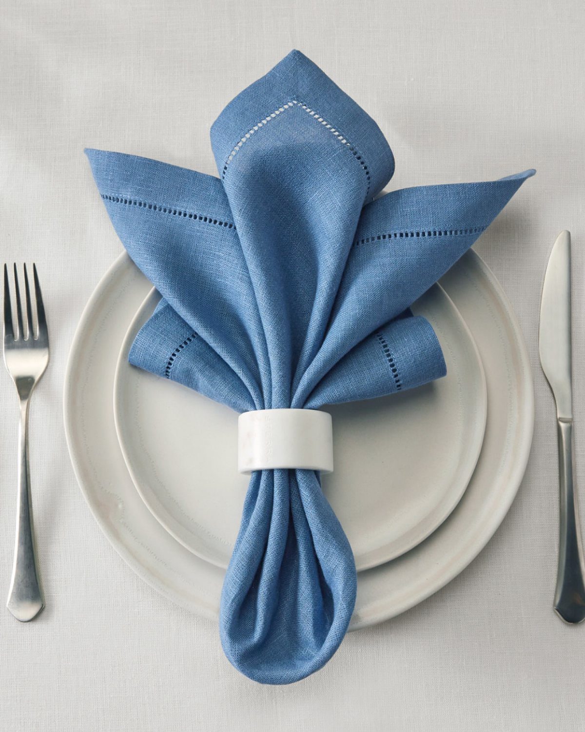 A blue fabric napkin in a white ring on a white plate with silverware.