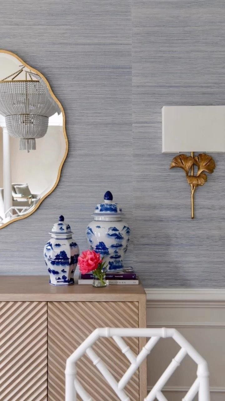 Light blue textured wallpaper behind a wooden sideboard with blue and white ceramic ginger jars.