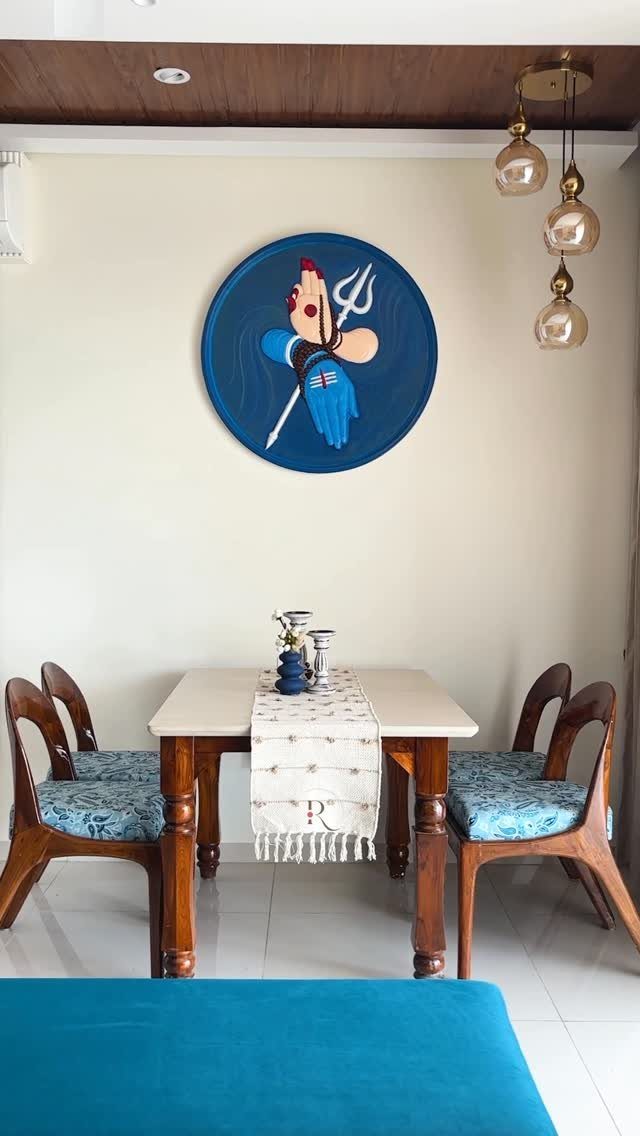 Dining table with blue upholstered chairs and circular blue wall art in a bright room.