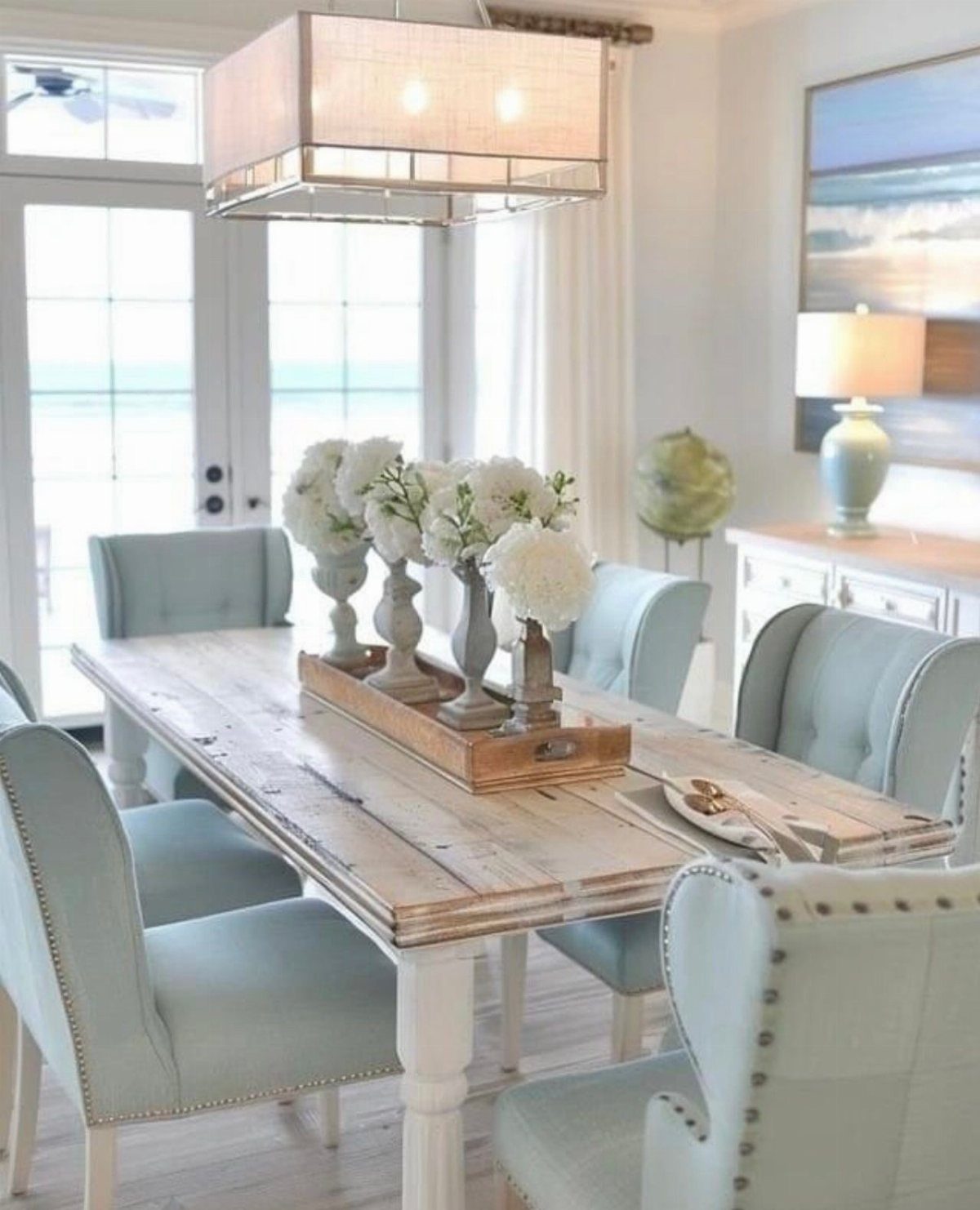 Light blue dining chairs surround a wooden table in a bright coastal-themed dining room.