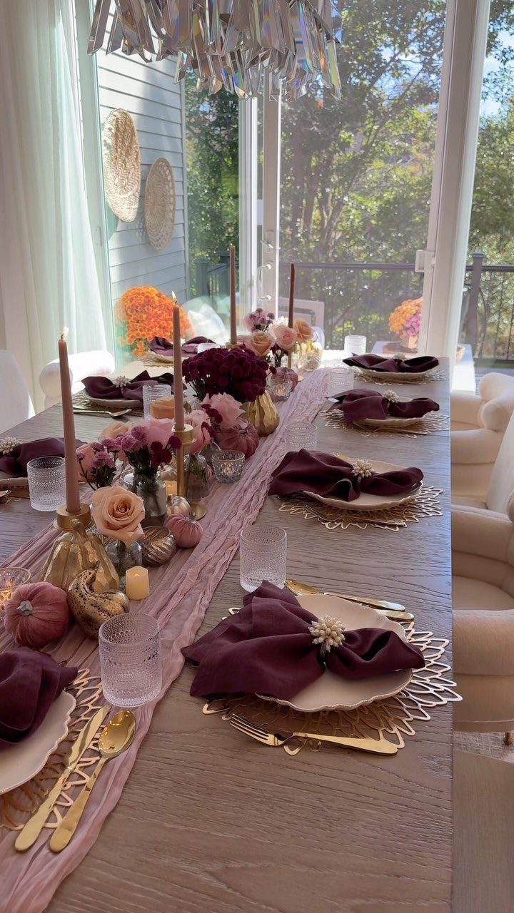 A long wooden dining table decorated with flowers, taper candles, and burgundy napkins for a formal meal.