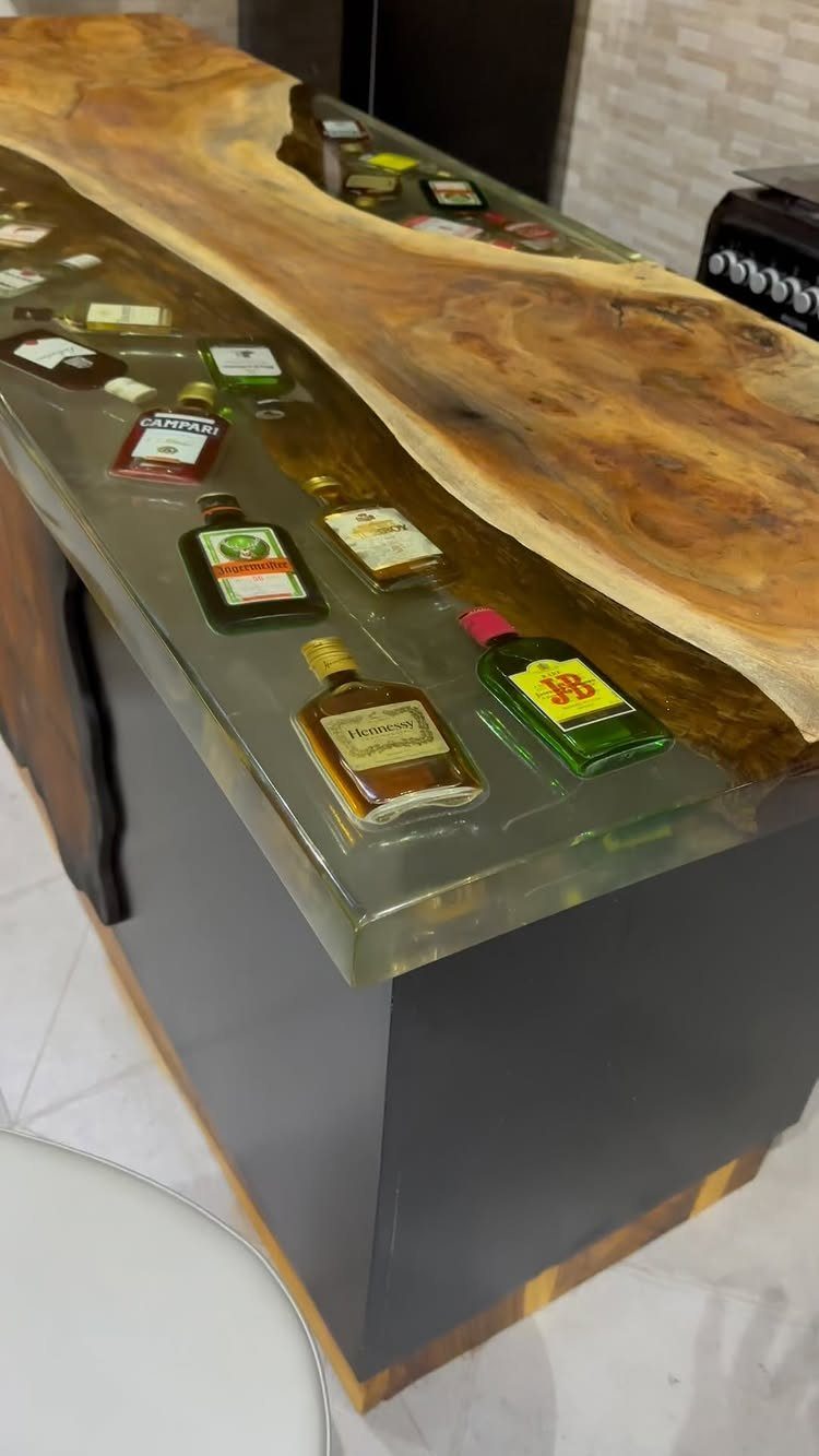 A bar counter with a live edge wood slab and a grey epoxy resin river top.