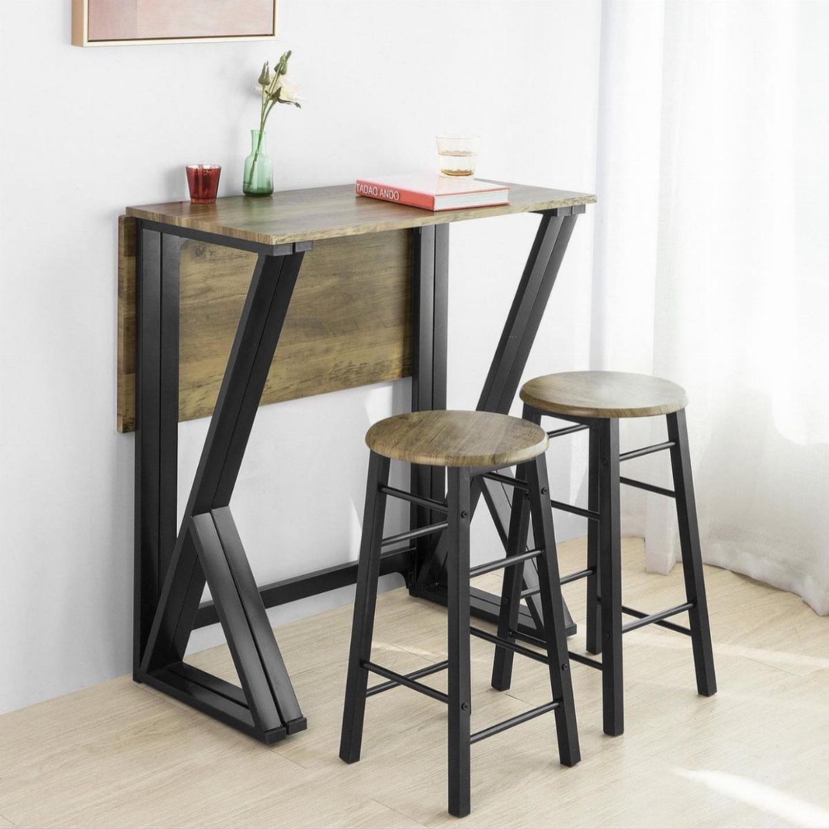 A foldable wooden bar table with black metal legs and two matching bar stools.