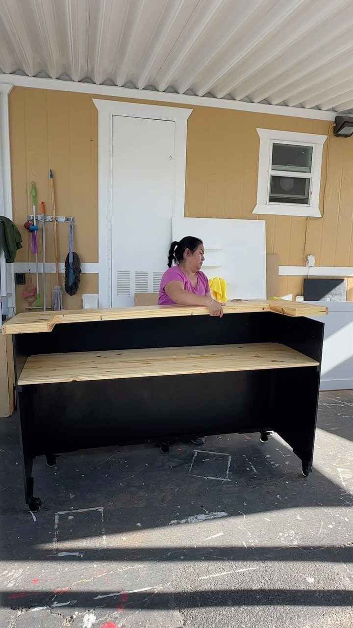 A woman standing behind a black portable bar with a light wood countertop on wheels.