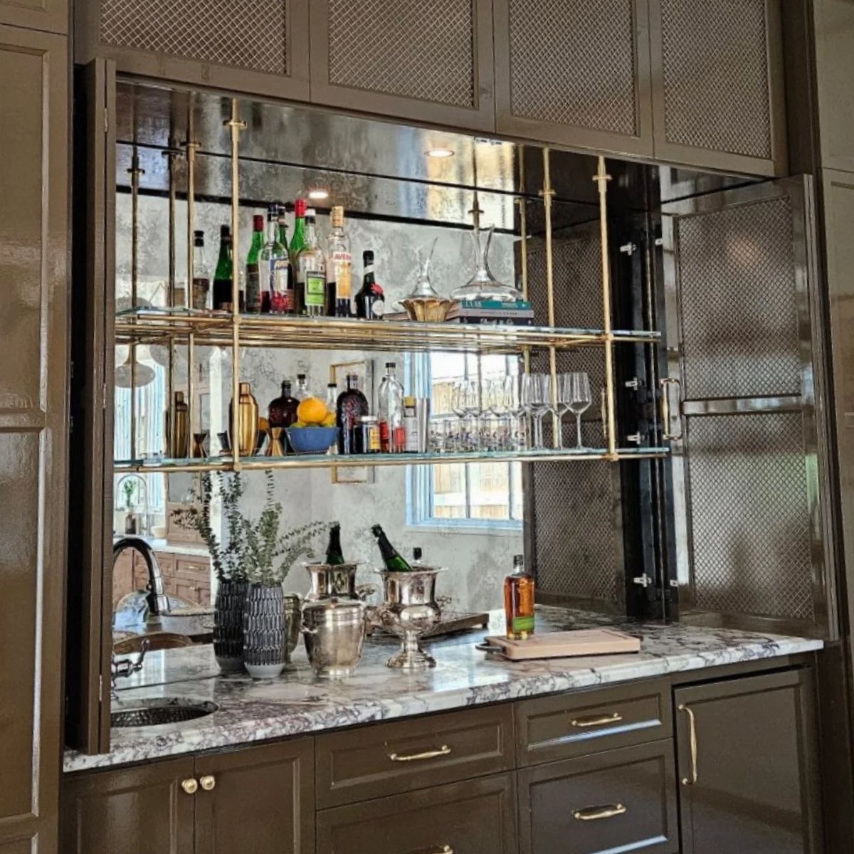 A sophisticated home bar with marble countertops, gold shelving, and a large mirrored backsplash.