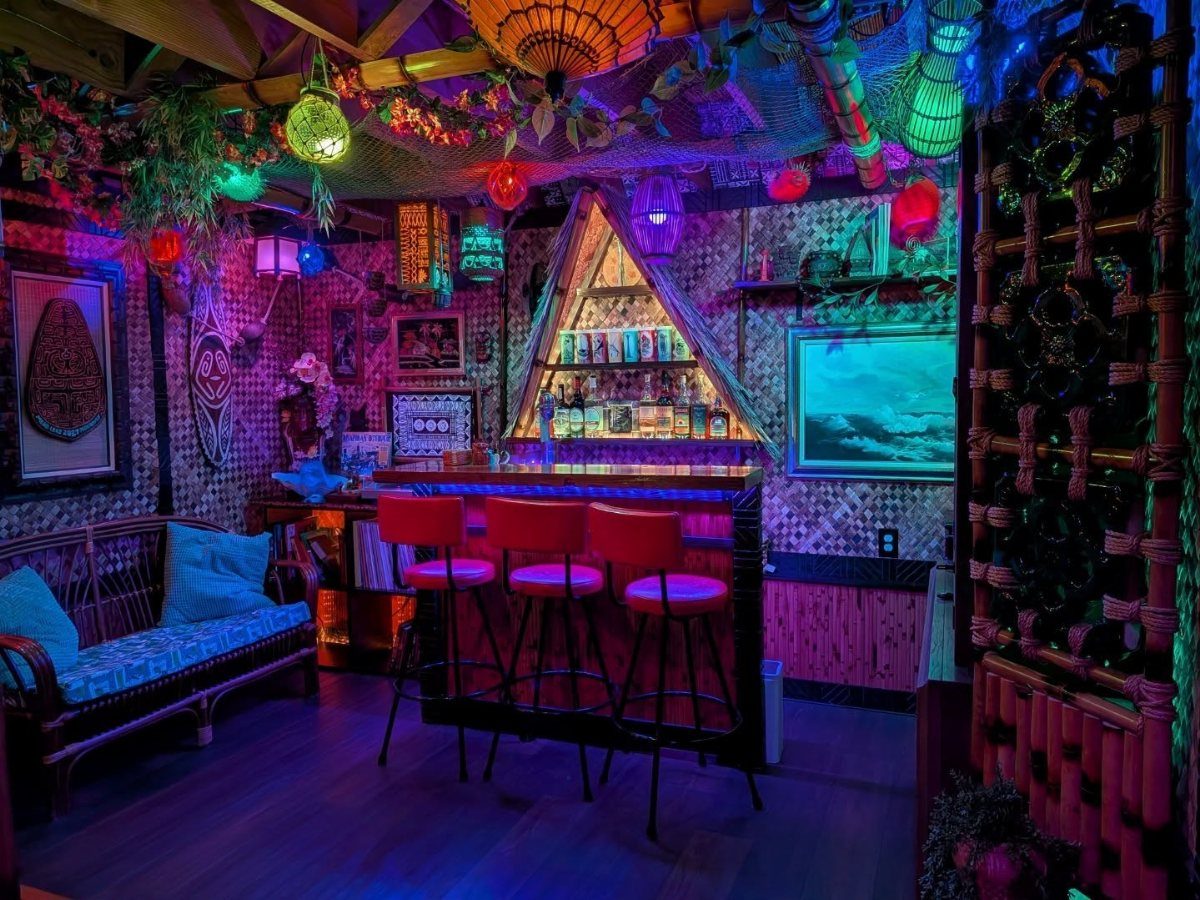 A vibrant tiki bar interior with neon lights, bamboo walls, and red bar stools.