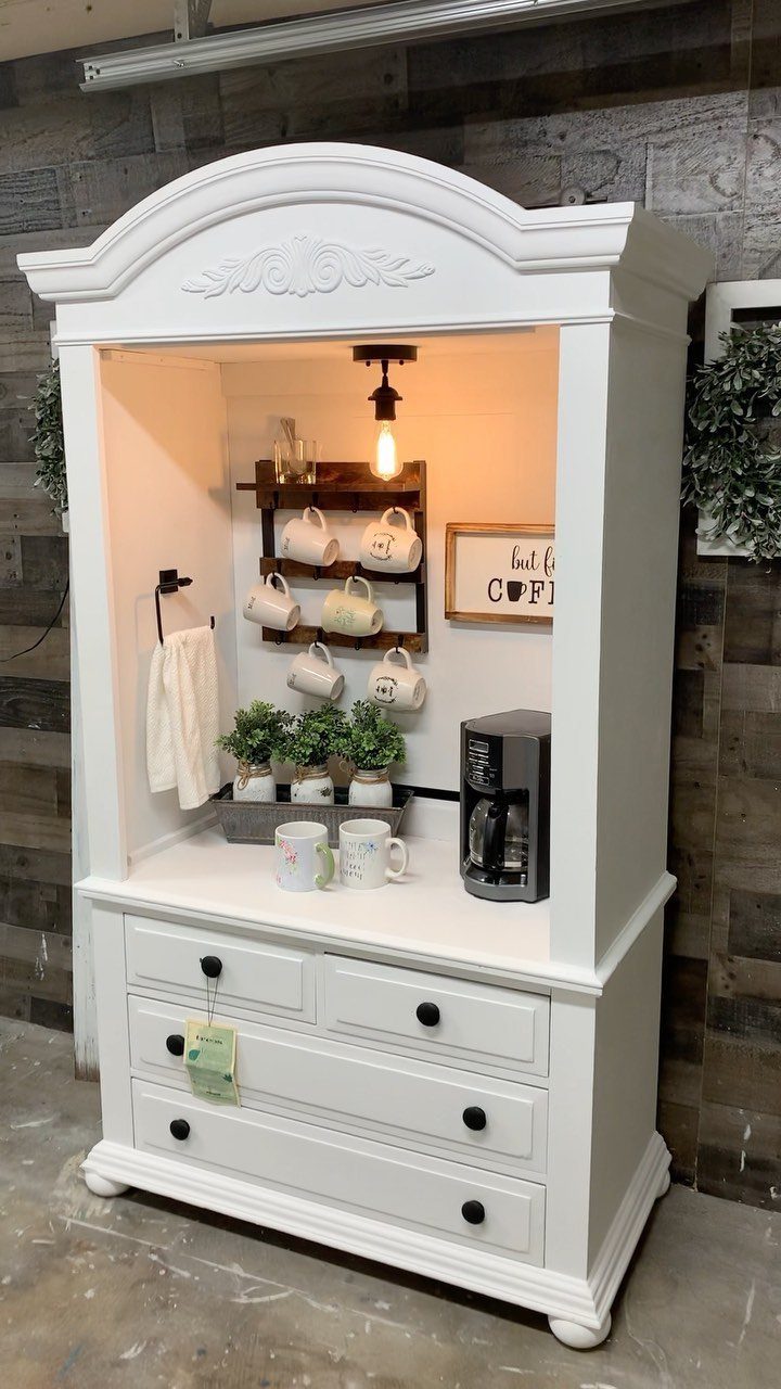 A white repurposed armoire serving as a coffee bar with mugs, plants, and a coffee machine.