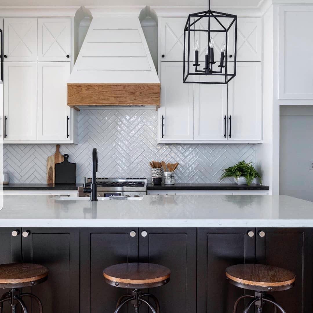 A large white marble kitchen island with dark cabinets and three wooden stools in a modern kitchen.