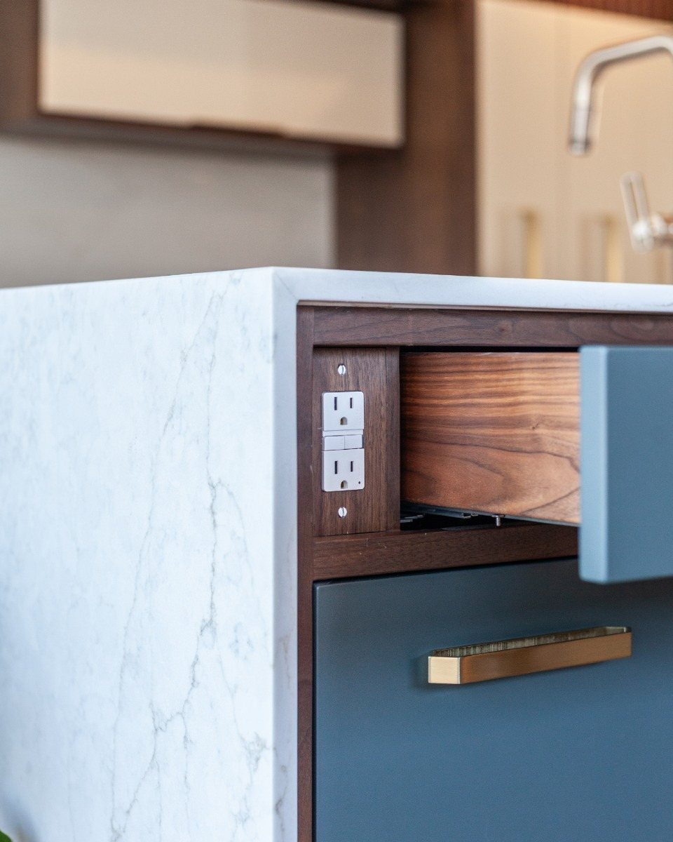 A close-up of a kitchen island corner showing a white marble countertop and a built-in electrical outlet.