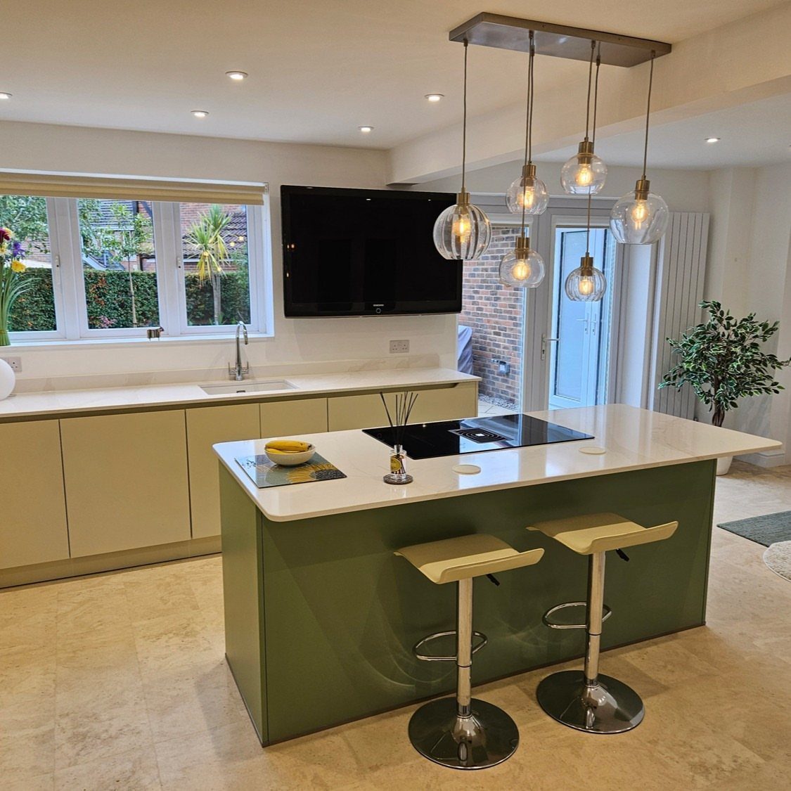 A green kitchen island with a white countertop and two bar stools in a bright kitchen.