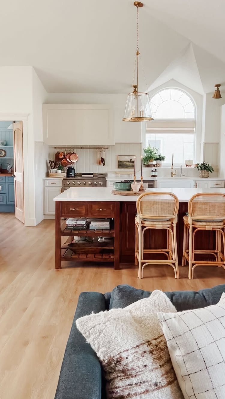 Wooden kitchen island with open shelving and two rattan bar stools in a bright kitchen.