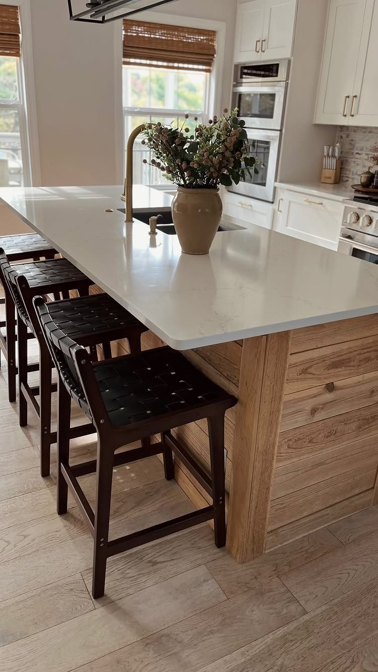 A large white kitchen island with light wood paneling and three dark wooden barstools.
