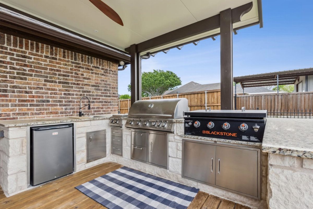A built-in outdoor kitchen with a stainless steel grill and a Blackstone griddle integrated into stone countertops.