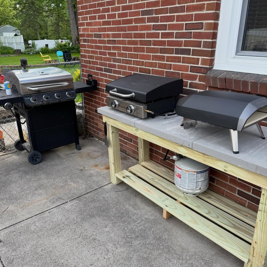A black Blackstone griddle sits on a wooden outdoor kitchen counter next to a stainless steel grill.