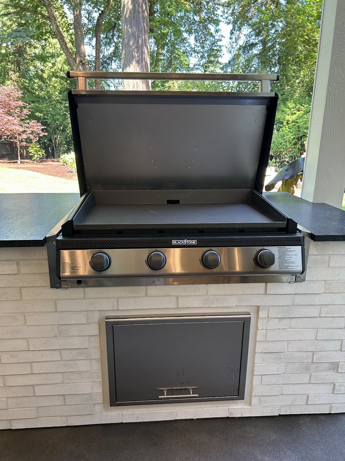 A Blackstone griddle built into a white brick outdoor kitchen island with a black countertop.