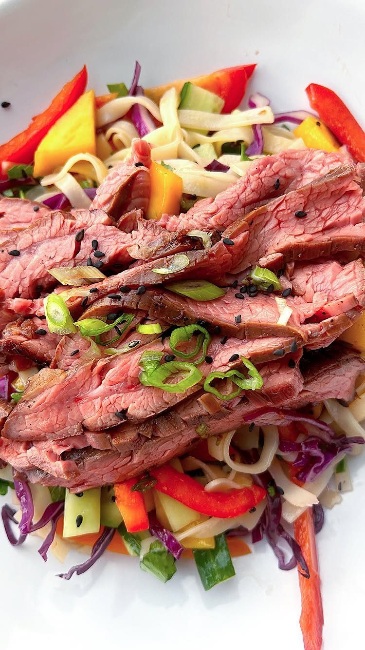 Sliced medium-rare steak served over a vibrant mango and vegetable salad.