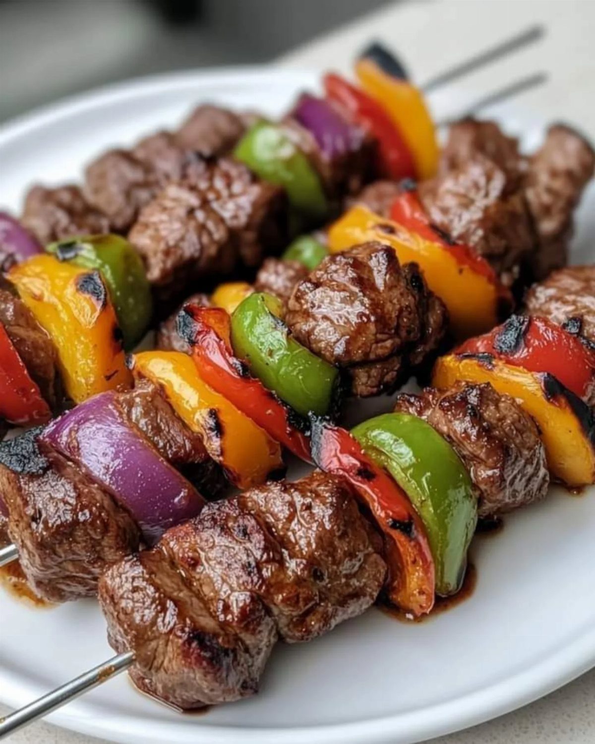 Grilled meat and vegetable skewers with beef, peppers, and red onion on a white plate.