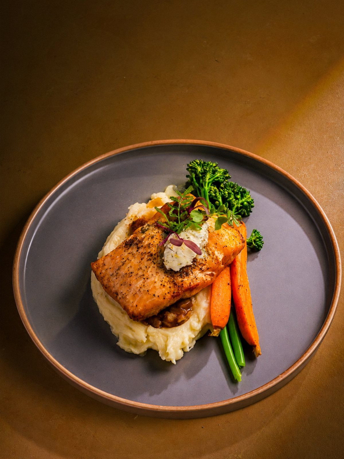 Grilled salmon fillet served with mashed potatoes and mixed vegetables on a dark plate.