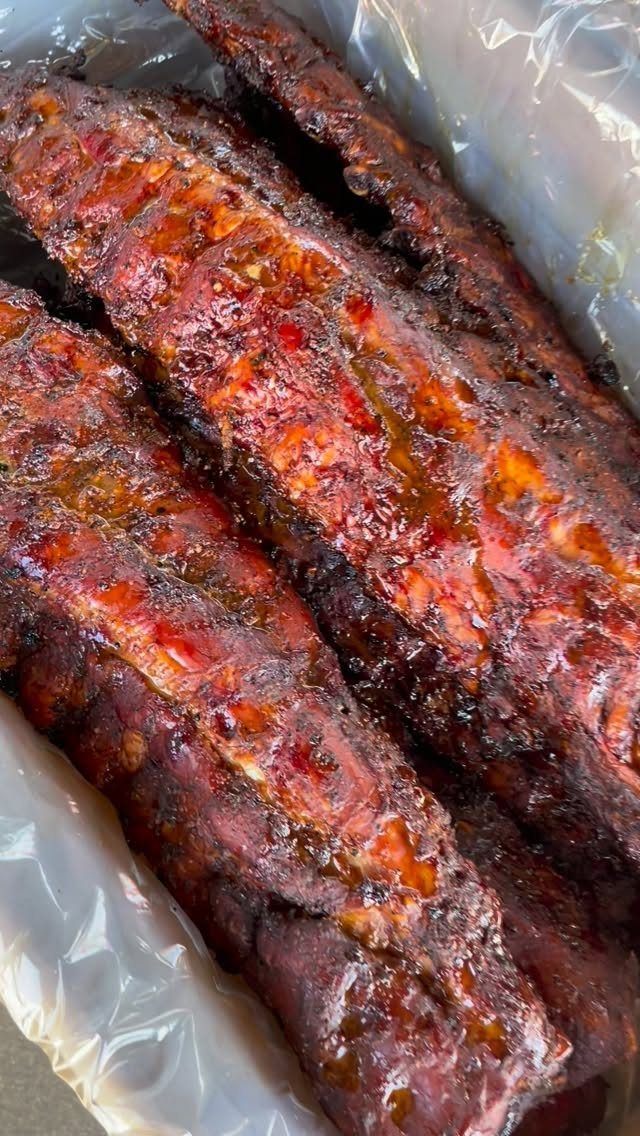 Glazed barbecue ribs with a shiny sauce resting in a plastic-lined container.