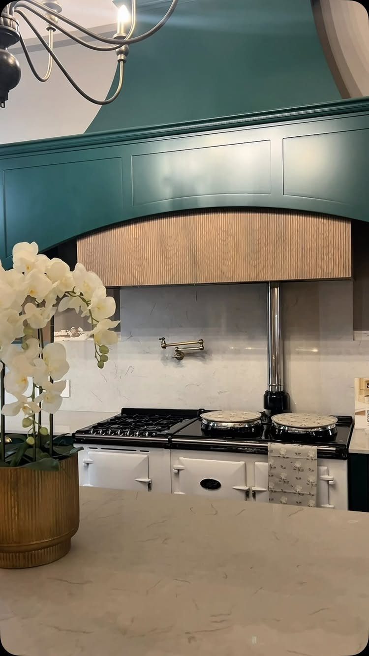 White AGA cooker under a teal range hood with white orchids in the foreground.