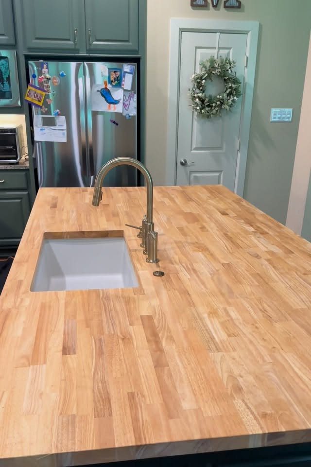 Butcher block wooden countertop on a kitchen island with a white sink and metal faucet.