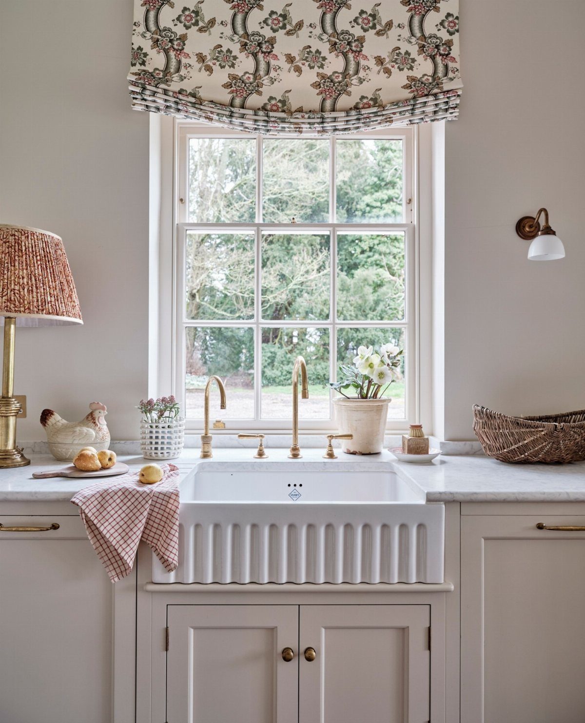 A white ribbed ceramic butler's sink with brass faucets positioned under a large window.