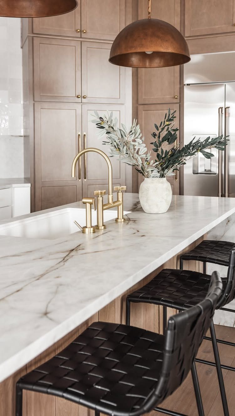 White marble countertop with grey veining on a kitchen island featuring a gold faucet and olive branches.