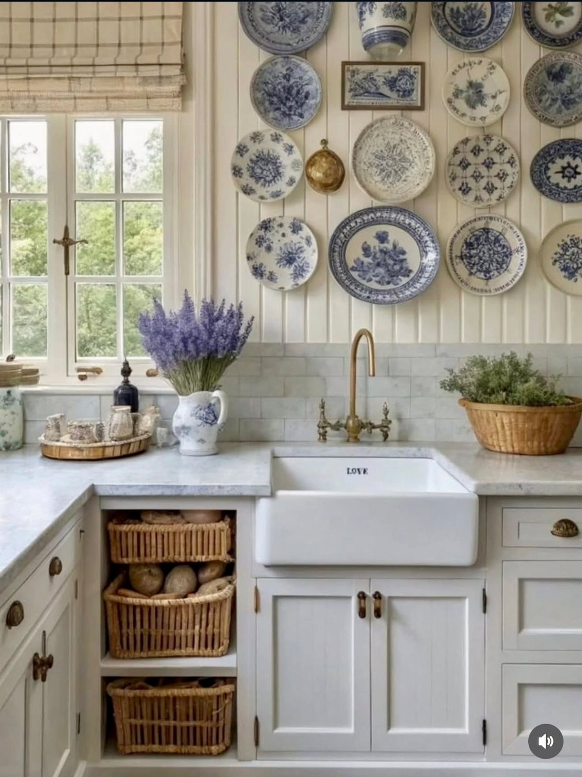 White kitchen with a farmhouse sink, brass faucet, and blue and white patterned plates on the wall.