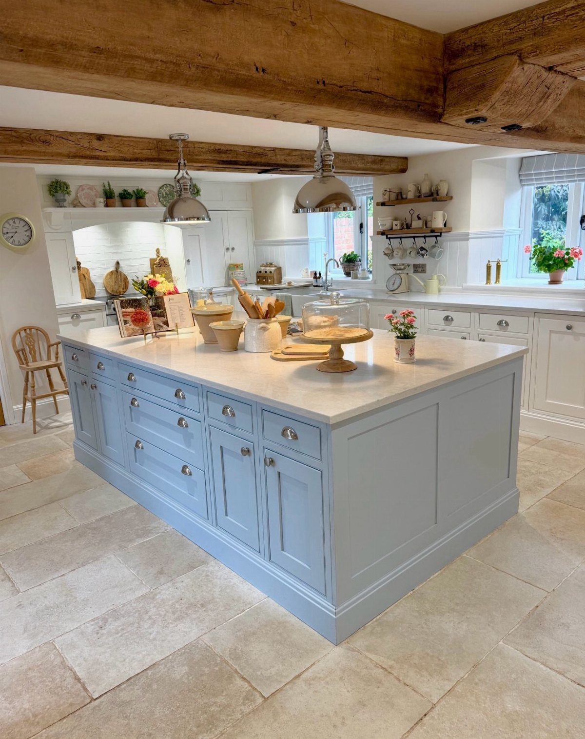 A large light blue kitchen island sits on stone tiles beneath heavy exposed wooden ceiling beams.