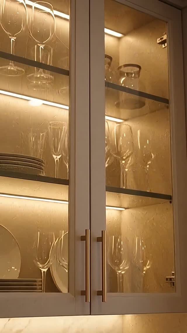 Glass-fronted kitchen cabinets with warm interior lighting displaying glassware and ceramic plates.
