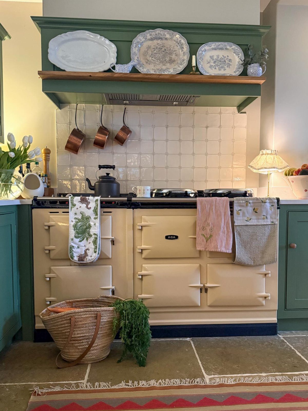 Cream AGA stove with copper pots and decorative plates in a green English style kitchen.