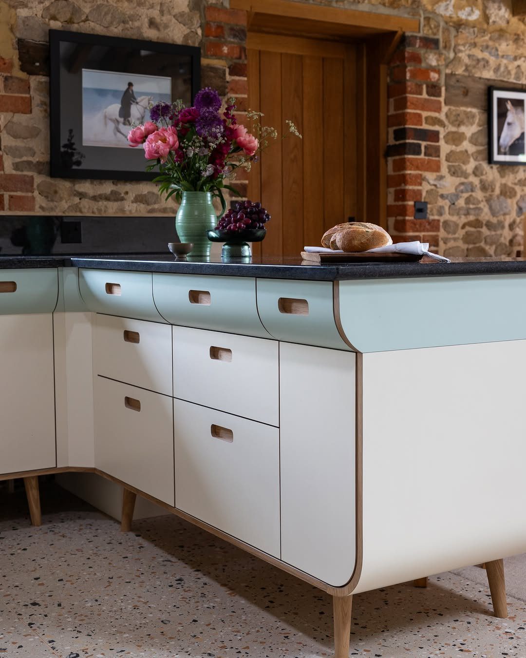 Cream and light blue kitchen cabinetry with rounded corners and wooden legs against a stone wall.