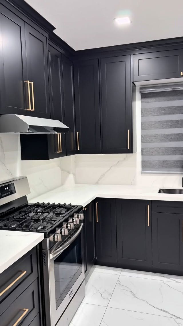 Black Shaker-style kitchen cabinets with gold handles and white marble countertops and backsplash.