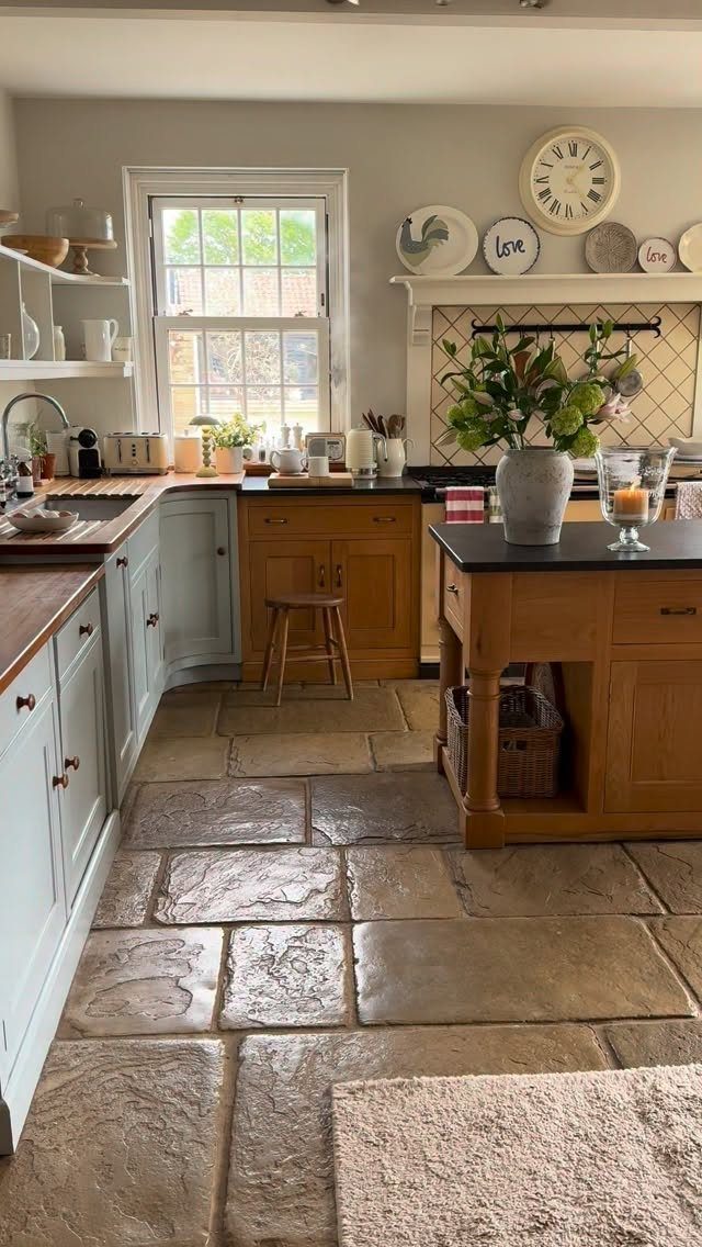 A rustic English style kitchen with blue cabinets, wooden counters, and large stone floor tiles.