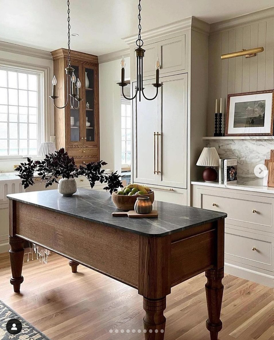 A large wooden kitchen island stands on light timber flooring in a bright, classic kitchen.