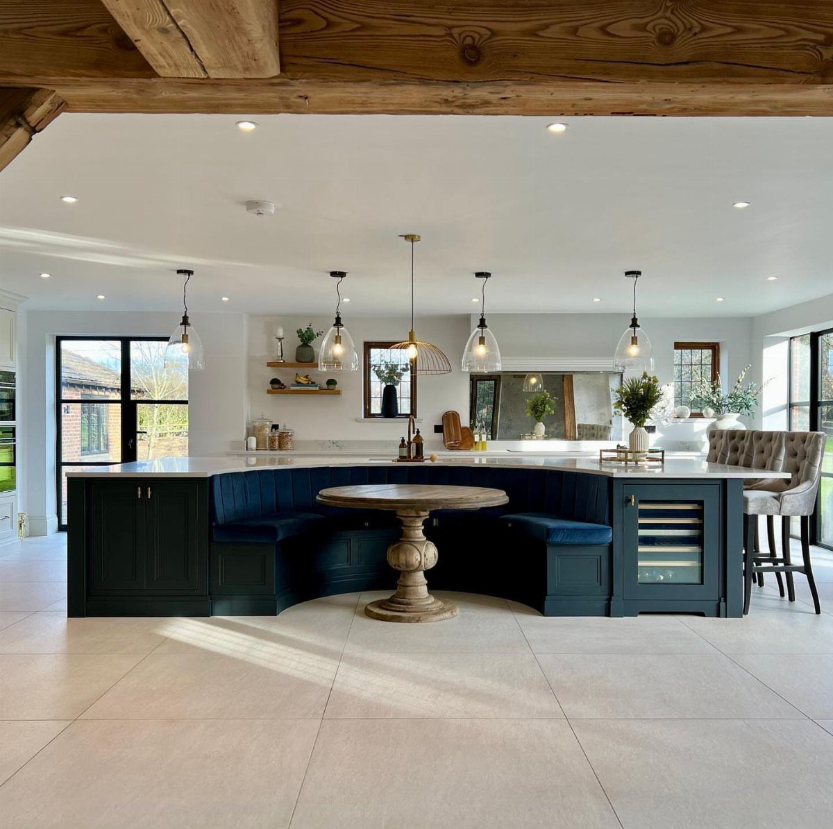 A large dark teal kitchen island with white countertops and grey tufted bar stools.