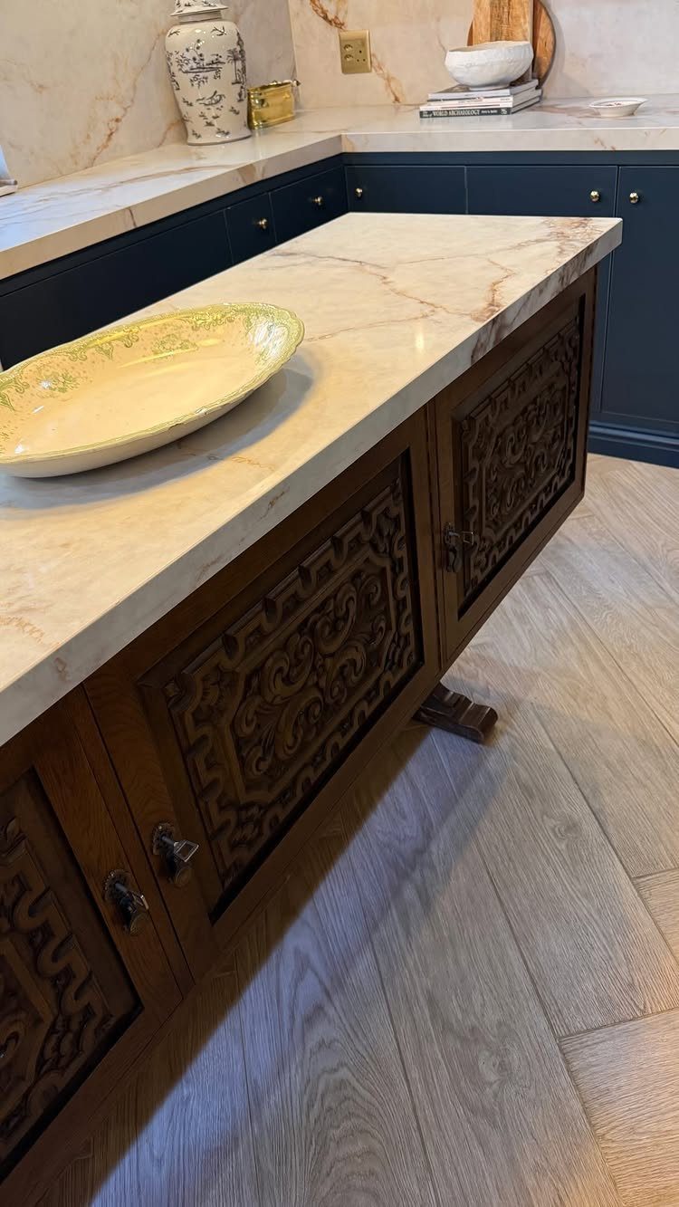 Ornate dark wood kitchen island with a white marble countertop and a yellow bowl.