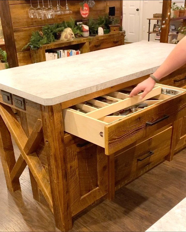 A hand pulls open a wooden drawer from a rustic farmhouse kitchen island.