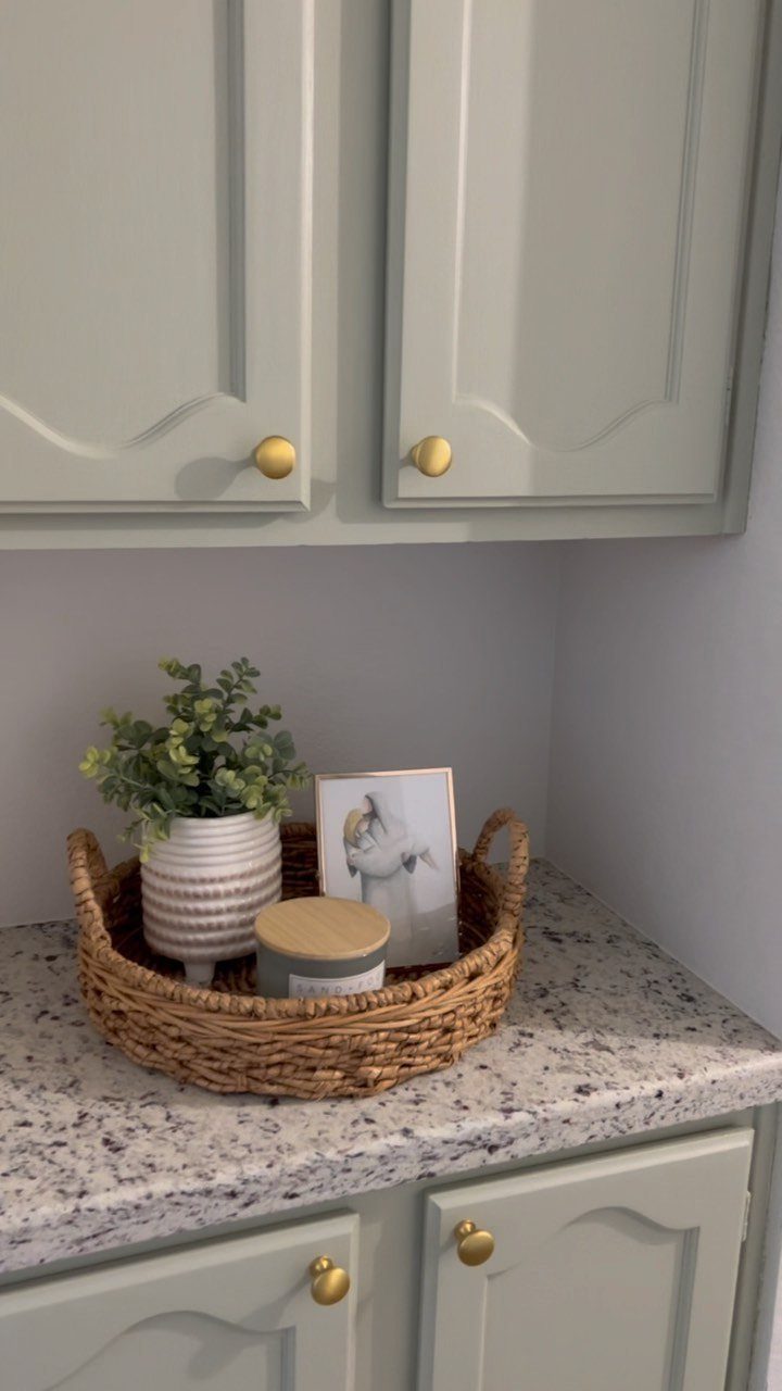 Green Kitchen Cabinets: 12 Ideas for Every Shade 7 Light sage green kitchen cabinets with gold hardware and a granite countertop with a decorative basket.