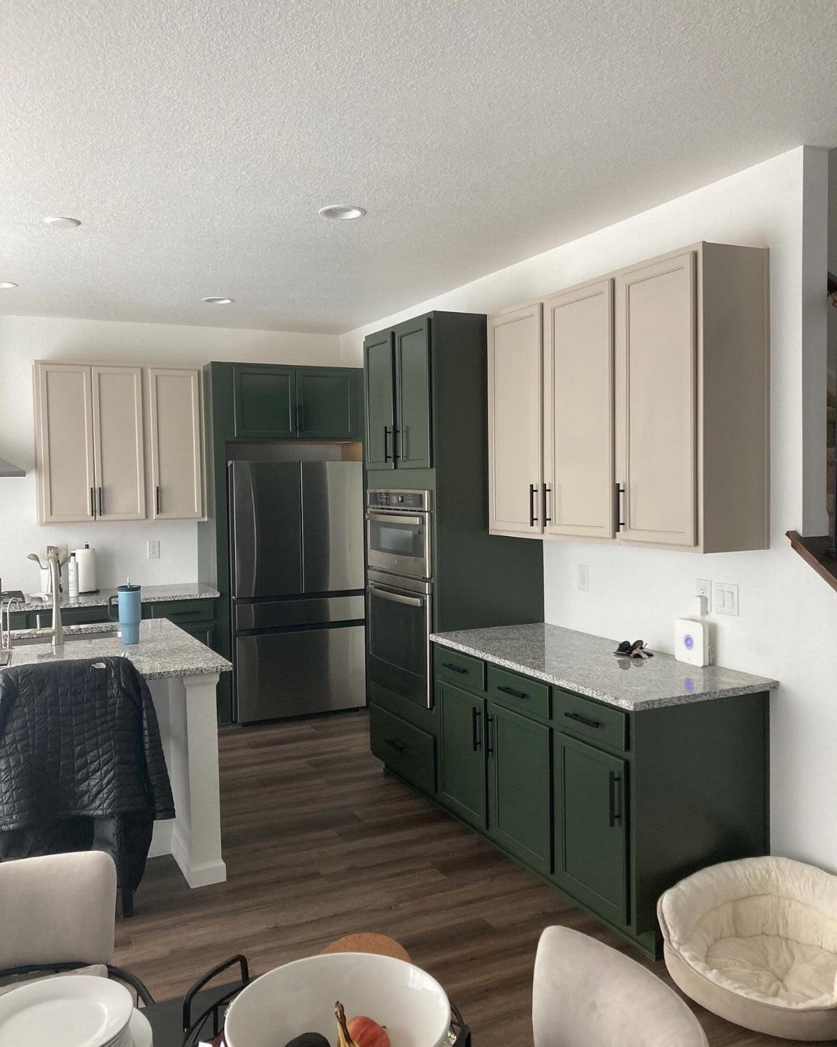 Green Kitchen Cabinets: 12 Ideas for Every Shade 4 Dark green lower kitchen cabinets paired with light beige upper cabinets and stainless steel appliances.