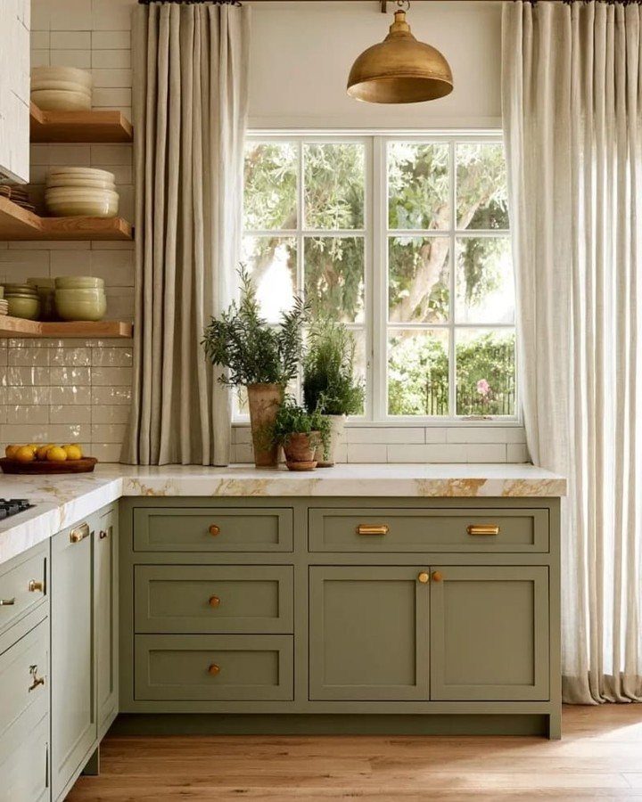 Green Kitchen Cabinets: 12 Ideas for Every Shade 8 Sage green kitchen cabinets with gold hardware and marble countertops near a bright window.
