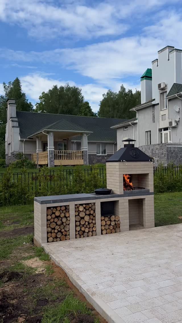 A brick outdoor barbecue station with firewood storage and a lit fire on a stone patio.