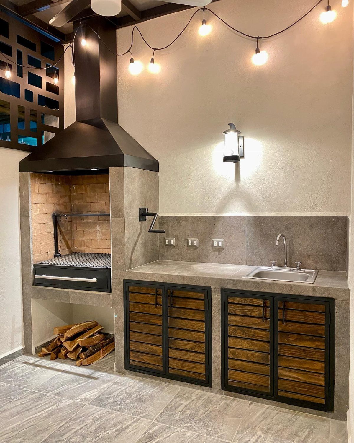 Built-in outdoor kitchen with a large black grill hood, stone countertop, sink, and wooden cabinets.