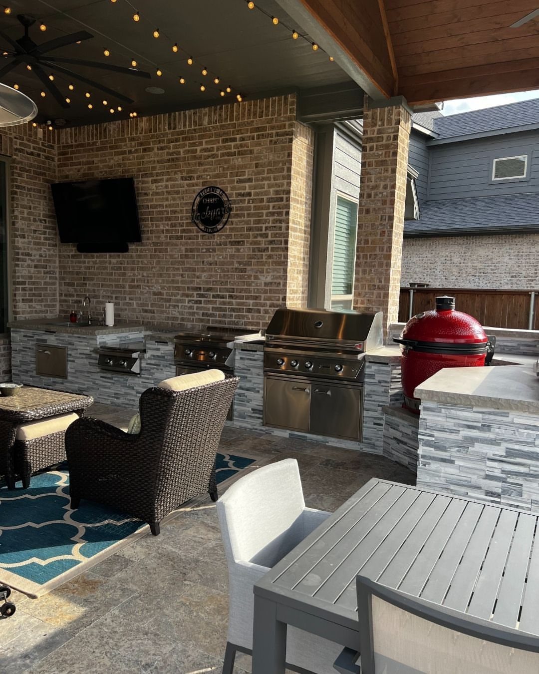 Stainless steel built-in grill and a red ceramic smoker on a stone patio.