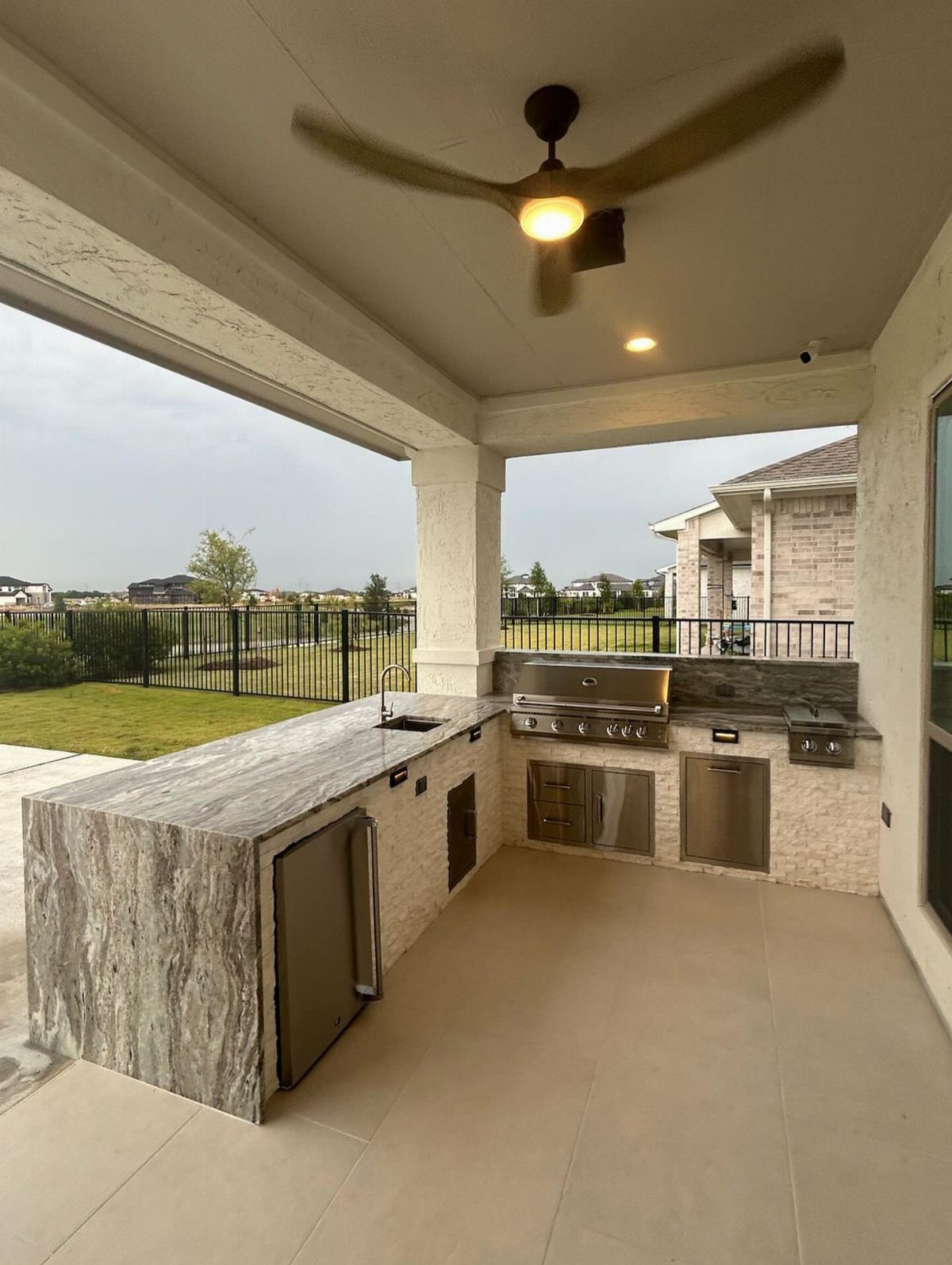 Modern outdoor kitchen with a stone breakfast bar, built-in grill, and stainless steel appliances under a patio.