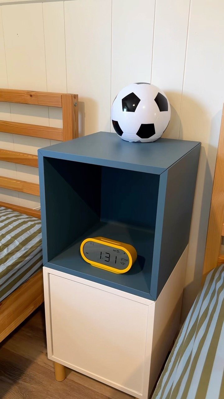A blue cubby nightstand with a soccer ball and yellow alarm clock next to a wooden bed.