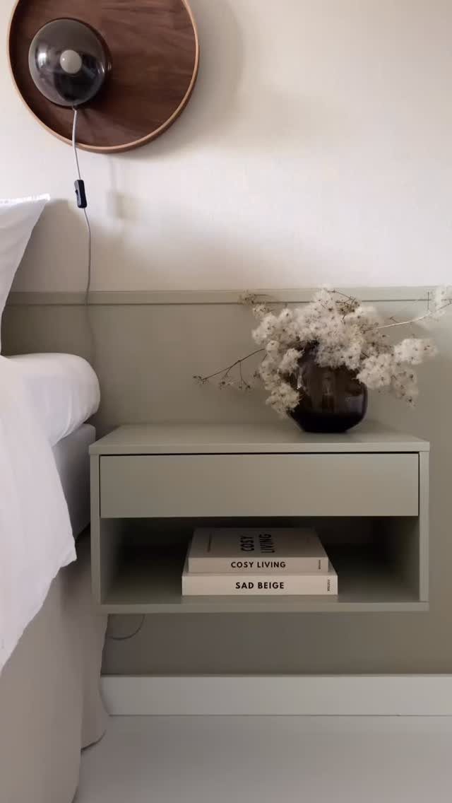 A sage green floating nightstand with dried flowers on top and books in the shelf.