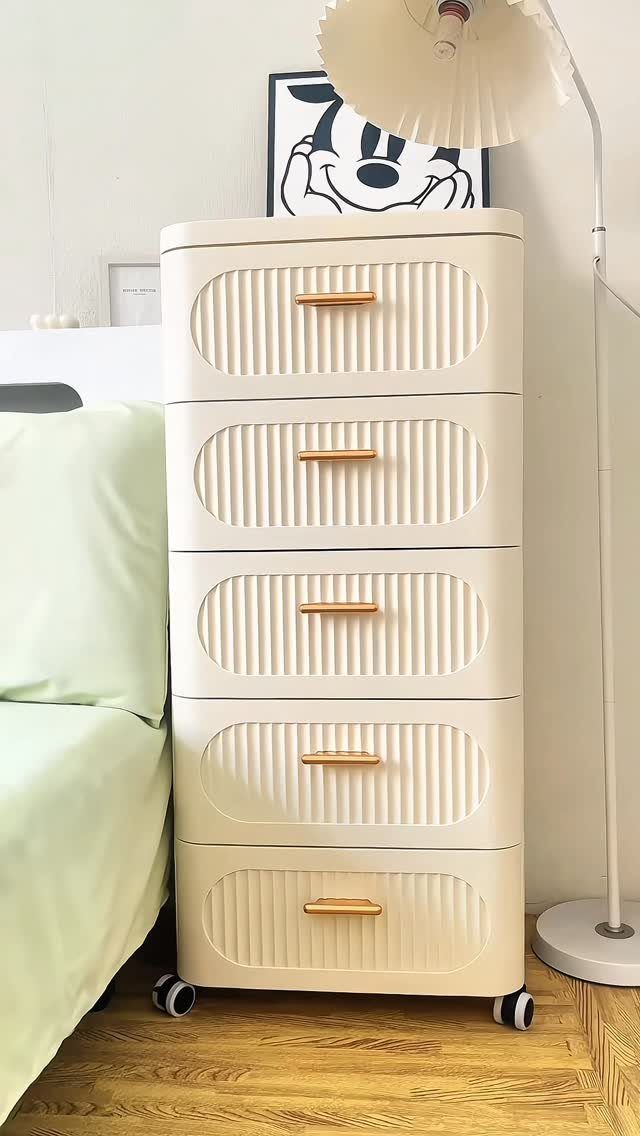 Cream ribbed rolling storage drawers with gold handles positioned next to a bed with green linens.