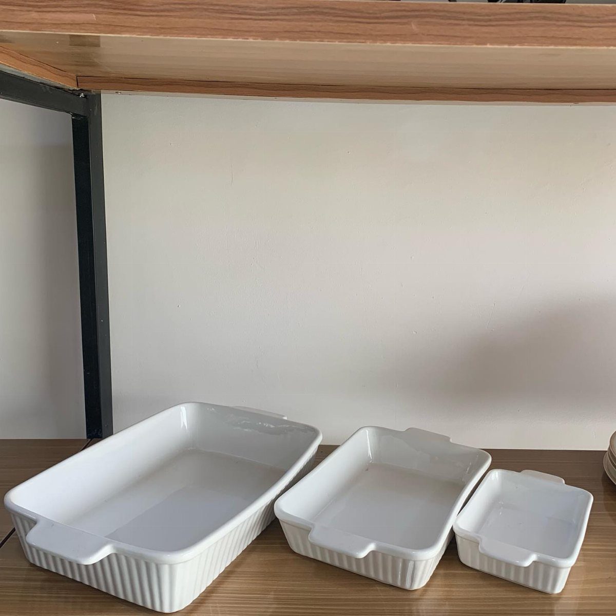 Three white ceramic baking dishes of different sizes arranged on a wooden shelf.