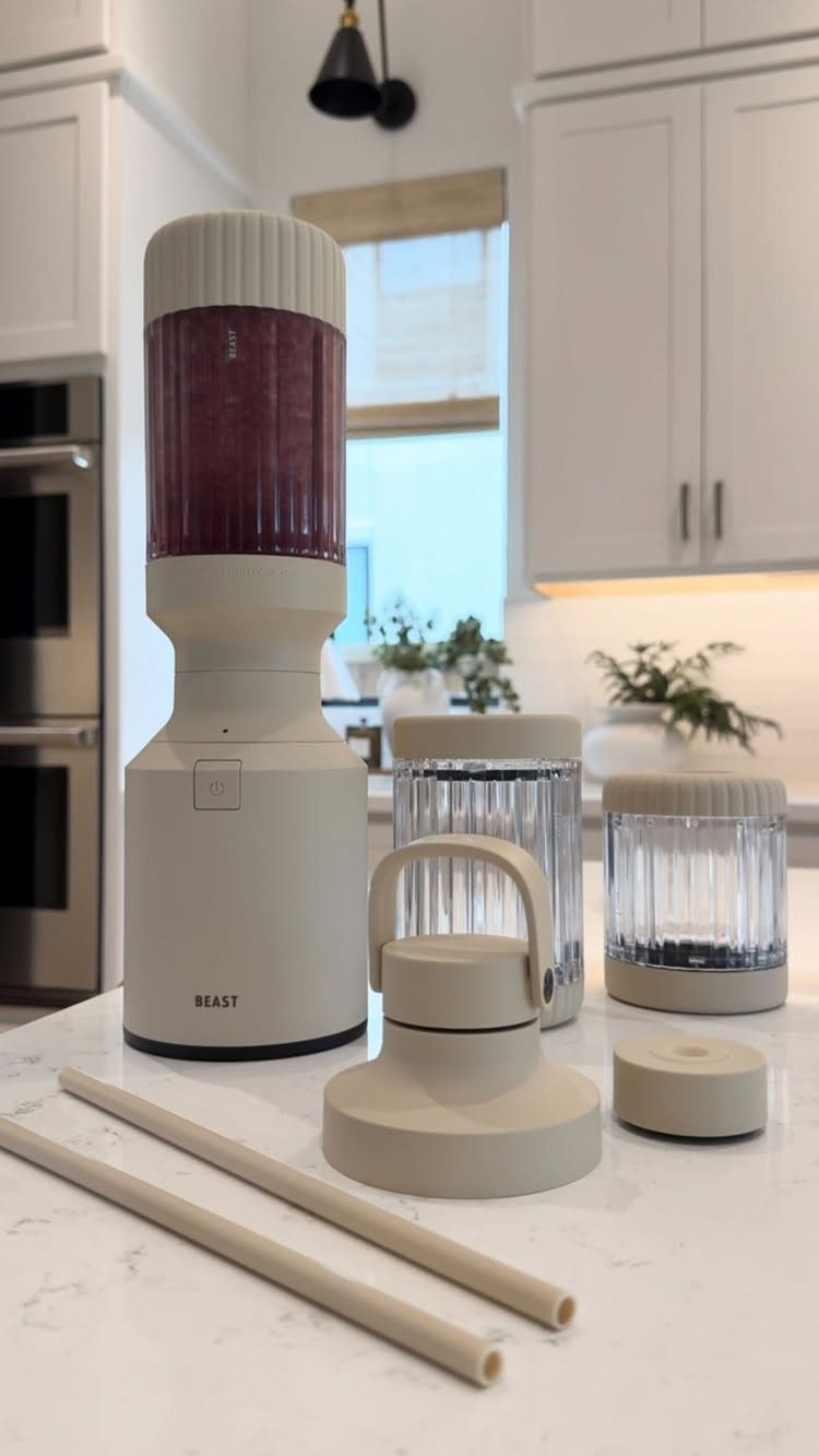 A beige Beast blender and its accessories sit on a white marble kitchen countertop.